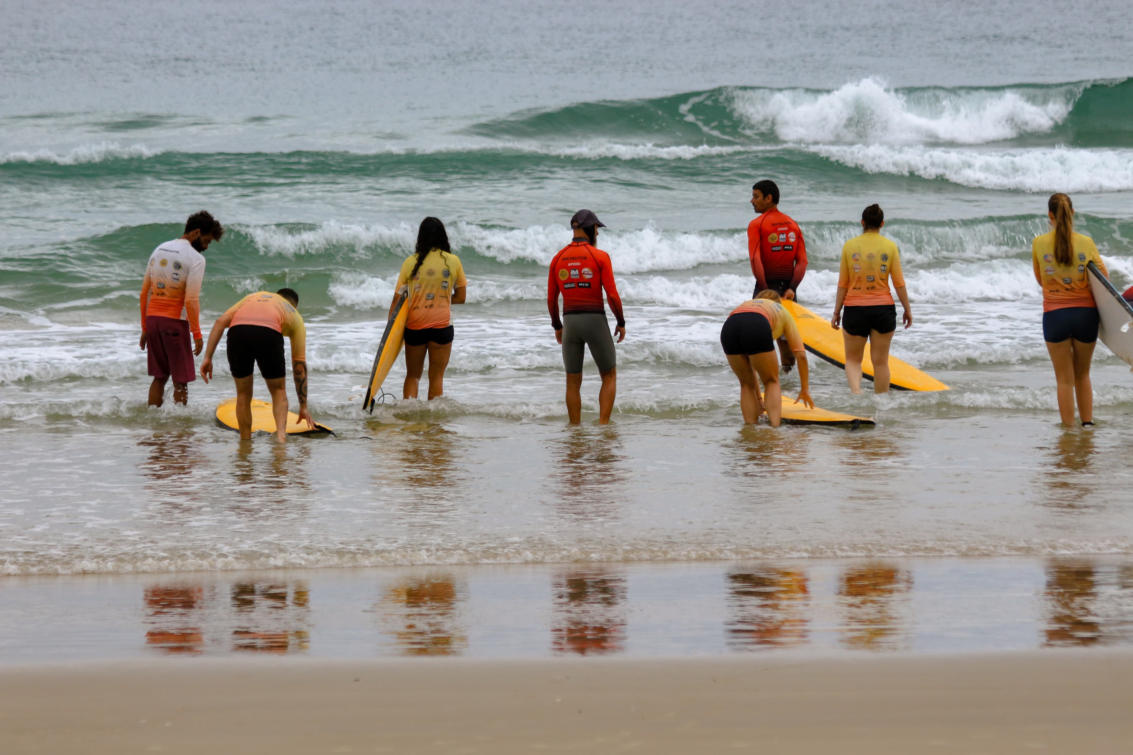 Instrutores auxiliando alunos a entrar no mar com as pranchas durante a aula