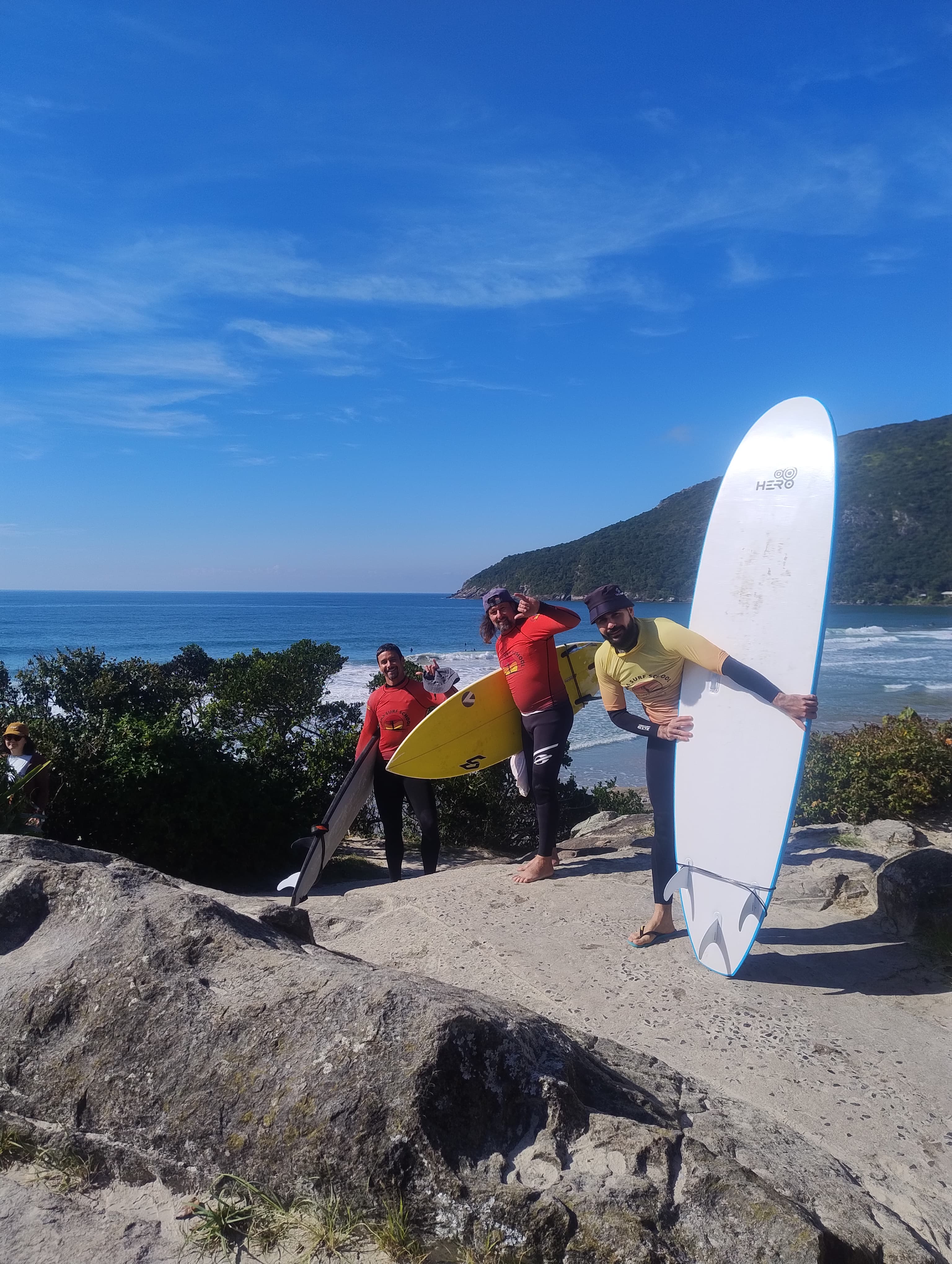 Instrutores da Forma Surf School posando com pranchas nas pedras da praia